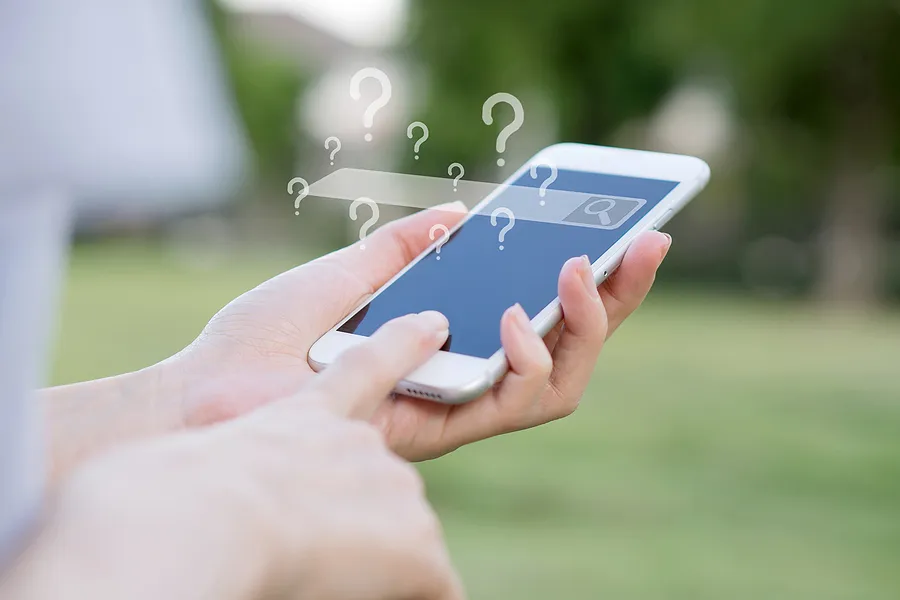 unas manos que sostienen un smartphone con la barra de búsqueda vacía y muchos signos de interrogación