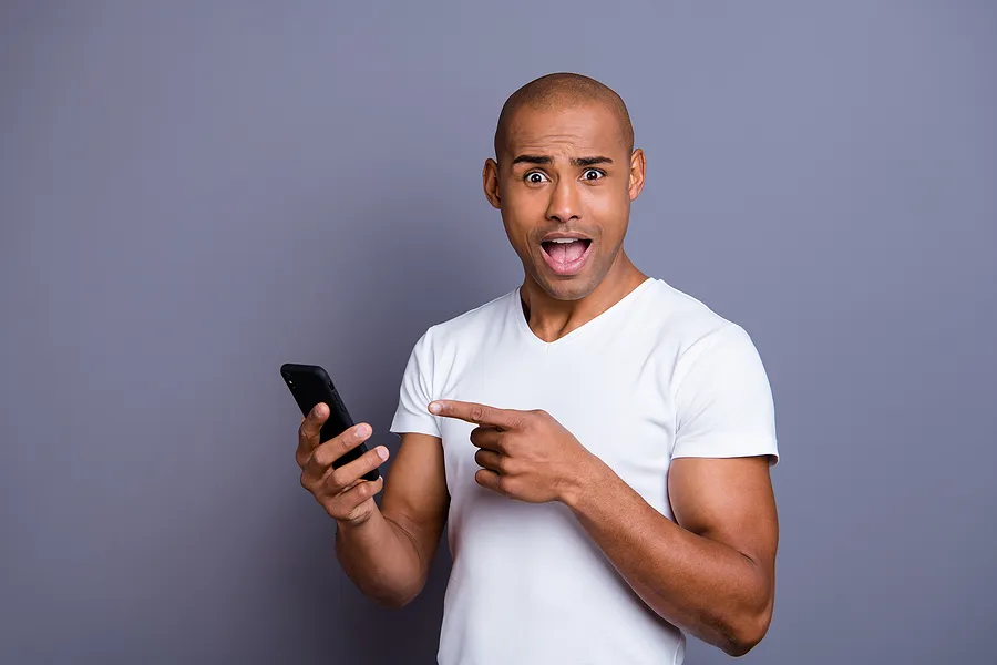 Un hombre que sostiene un teléfono móvil, con expresión de sorpresa