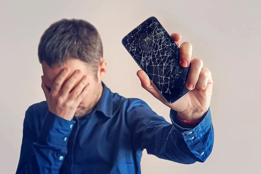Un hombre que se tapa los ojos y sostiene un teléfono móvil alejado de sí mismo.