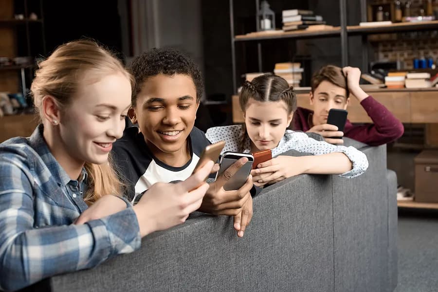 Cuatro adolescentes mirando sus teléfonos móviles.