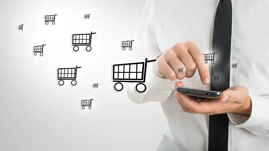 Un empresario utilizando un smartphone con iconos de carritos de la compra que simbolizan el comercio electrónico móvil y las compras por teléfono a través de Internet.
