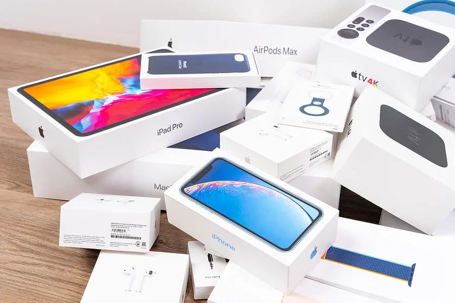 Una pila de cajas de productos de Apple, entre las que se incluyen el iPhone, el iPad Pro, los AirPods, el Apple Watch y el Apple TV, dispuestas sobre una superficie de madera.