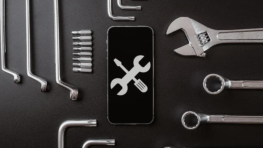 Herramientas de diagnóstico y concepto de reparación de teléfonos inteligentes, con la pantalla del teléfono mostrando el icono de una llave inglesa y un destornillador rodeados de herramientas metálicas.