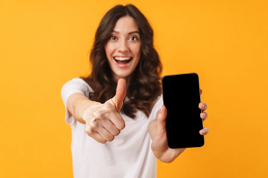 Mujer sonriente que sostiene un smartphone y levanta el pulgar, lo que simboliza que el proceso de verificación y certificación del teléfono se ha completado con éxito.