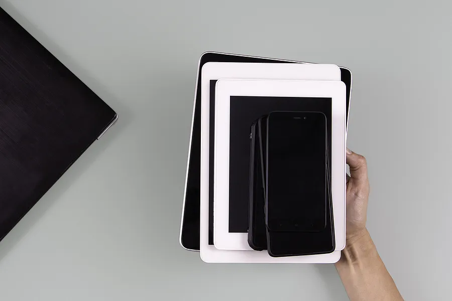 Una mano que sostiene varios dispositivos móviles apilados, entre ellos smartphones y tabletas, lo que simboliza el crecimiento del mercado y las tendencias futuras de los teléfonos reacondicionados.