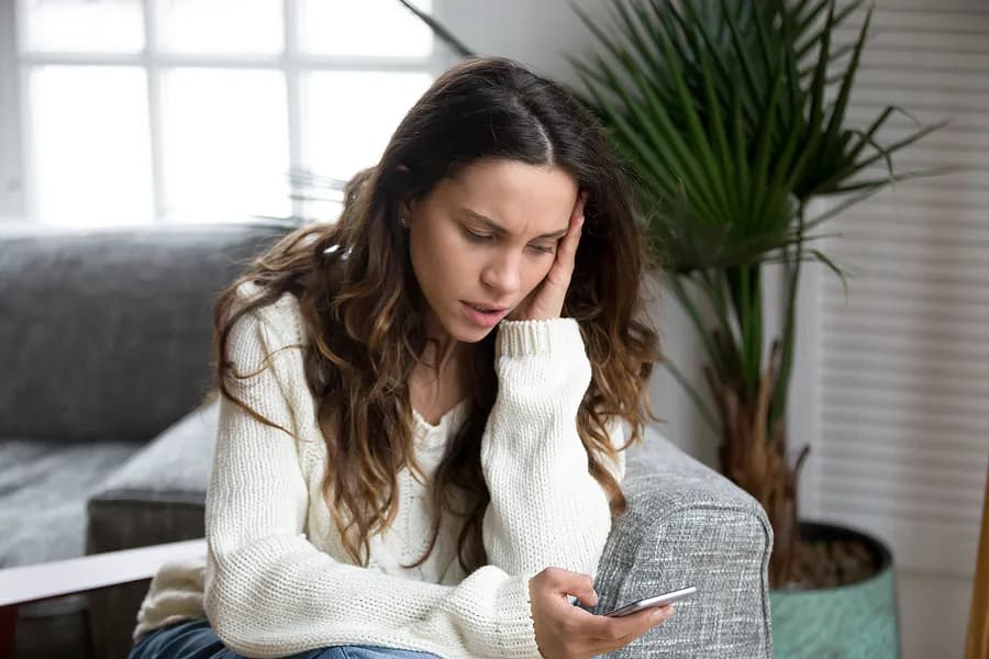 Una mujer preocupada mirando su smartphone, lo que ilustra la importancia de consultar los informes de teléfonos de segunda mano y comprender el historial del dispositivo antes de comprarlo.