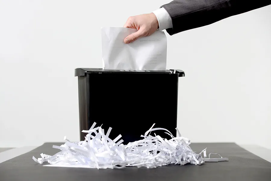 Imagen en la que se ve cómo se introducen documentos a mano en una trituradora de papel, lo que ilustra la destrucción certificada de datos y la eliminación segura de información confidencial.